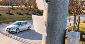 Roadside automatic license plate reader mounted on a utility pole overlooking a parking area.
